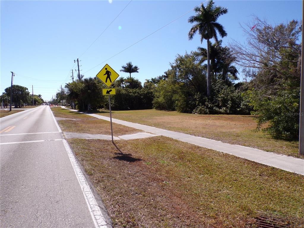 A roadside view of a vacant grassy lot with a pedestrian crossing sign and sidewalk — 711 COOPER STREET, PUNTA GORDA, FL
