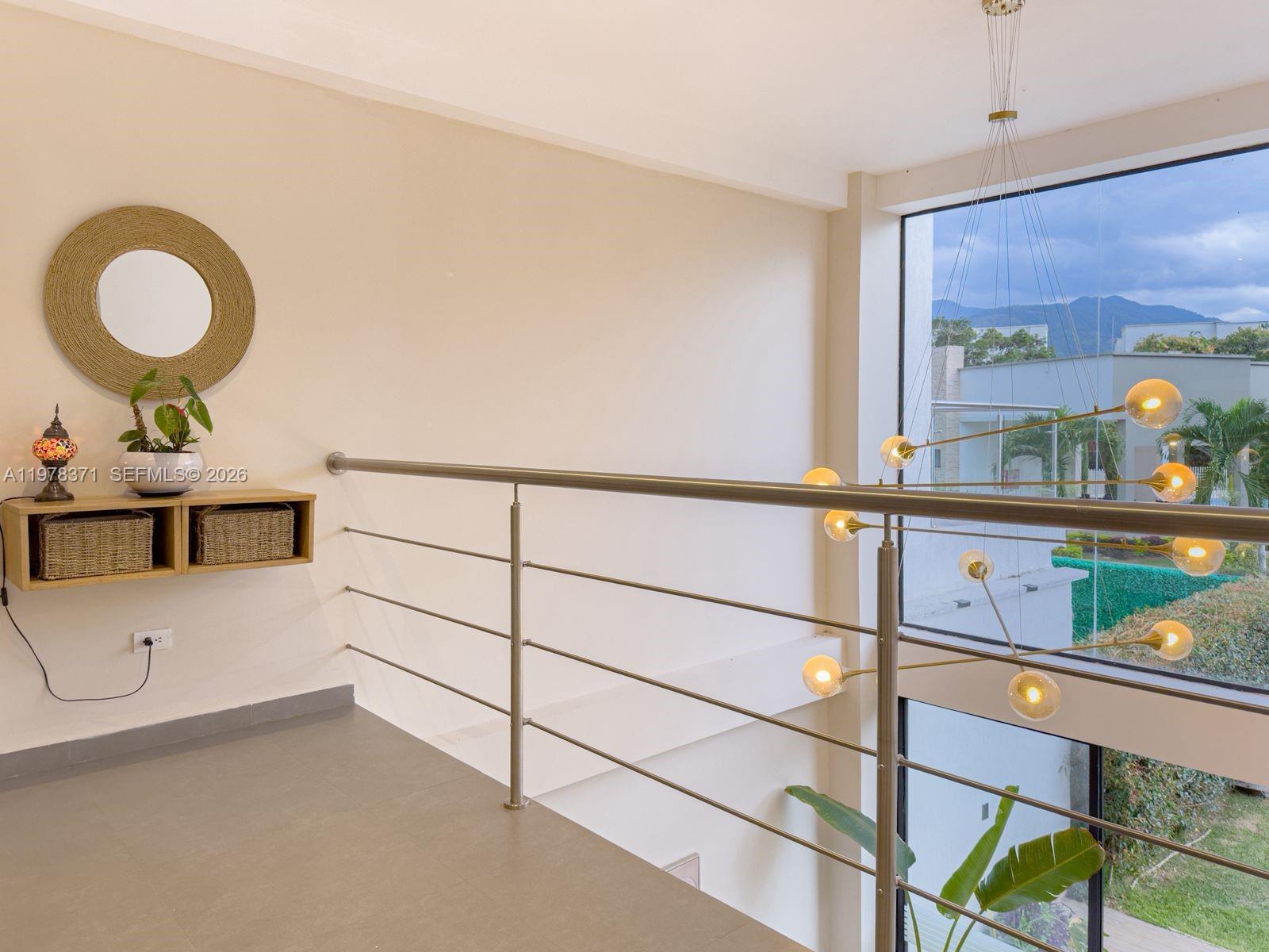 A modern mezzanine landing features a metal railing, a floating shelf, and a large chandelier — 150 Manantial Mercededs, 764001, FL