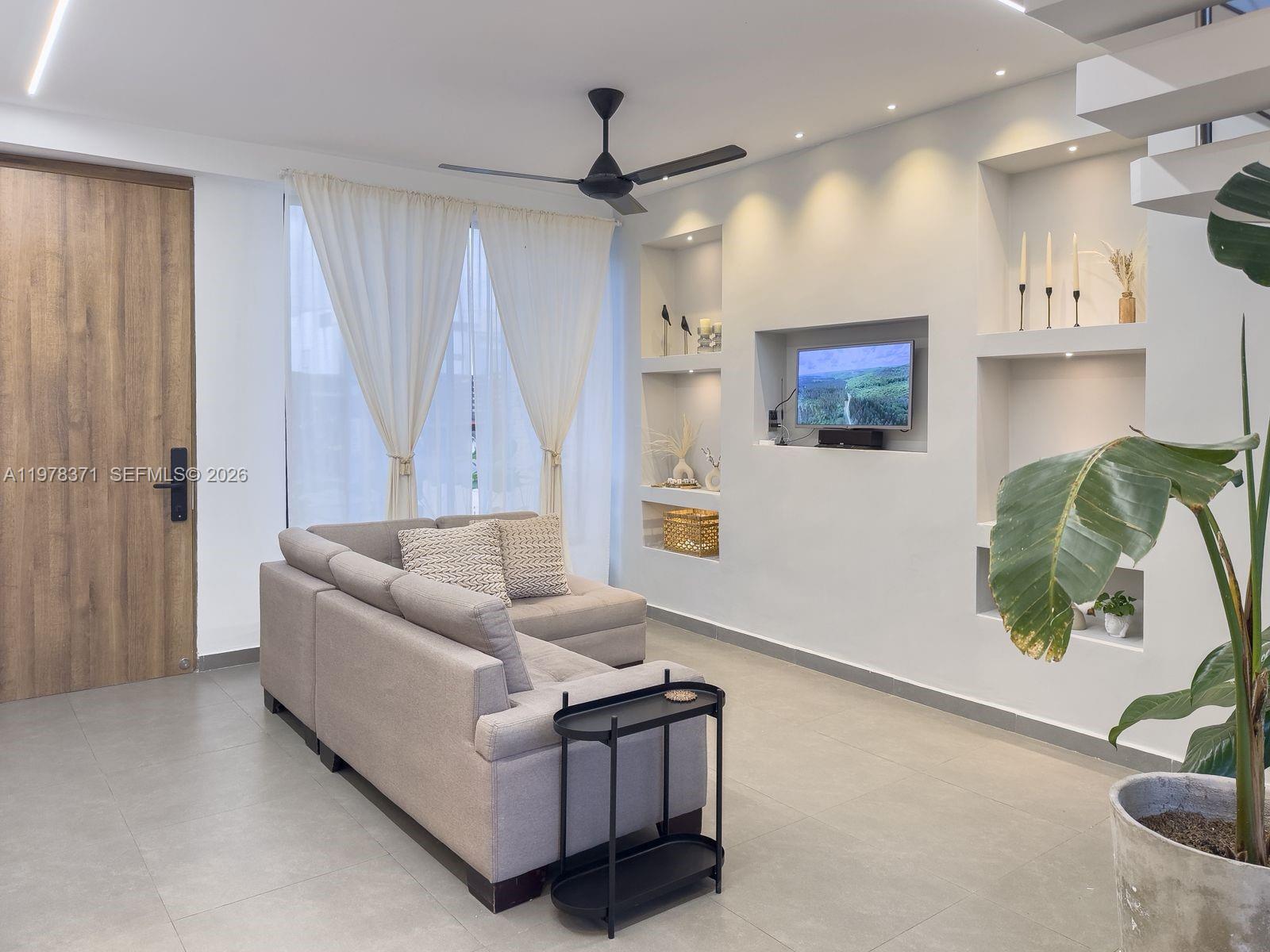 A modern living room features a gray sectional sofa, built-in wall niches, and tile flooring — 150 Manantial Mercededs, 764001, FL
