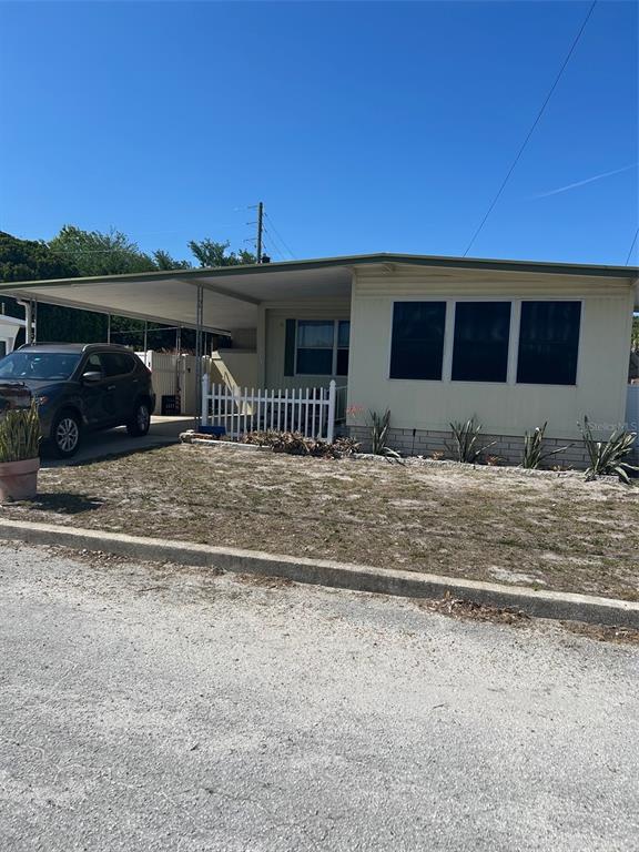 A single-story manufactured home with a carport, white picket fence, and a gravel driveway — 2574 ARBELIA STREET, CLEARWATER, FL