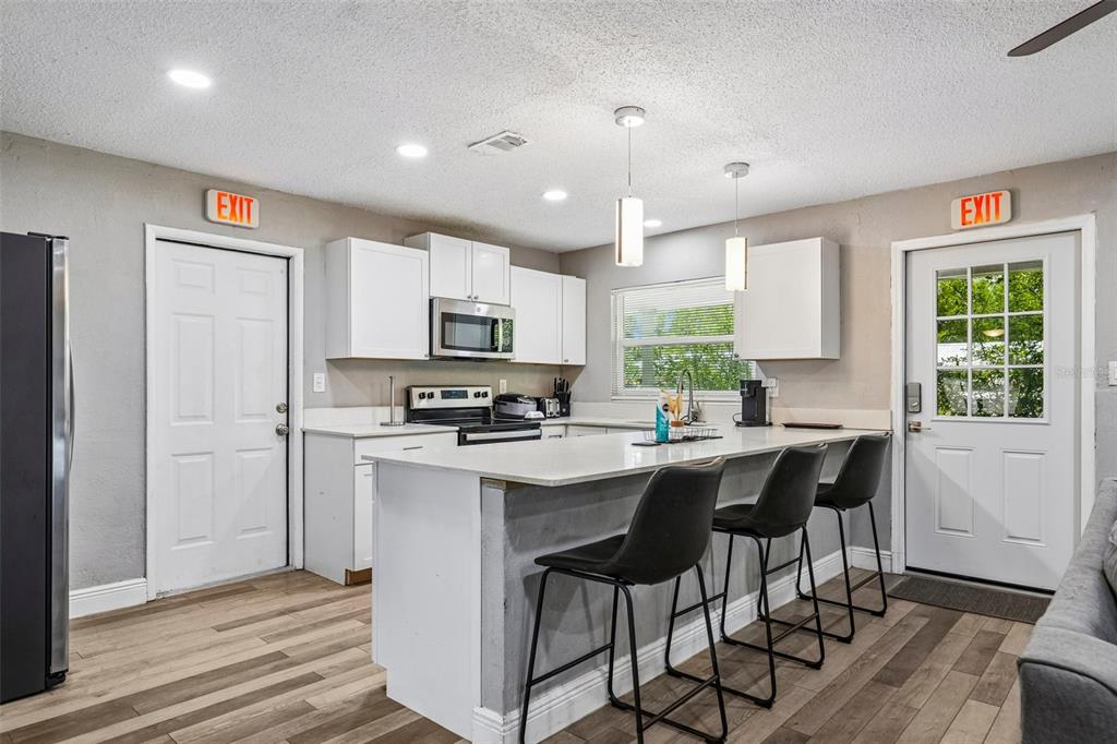 A kitchen features white cabinetry, a quartz-topped island with three stools, and two exit doors — 520 FAIRFAX LANE, APOLLO BEACH, FL