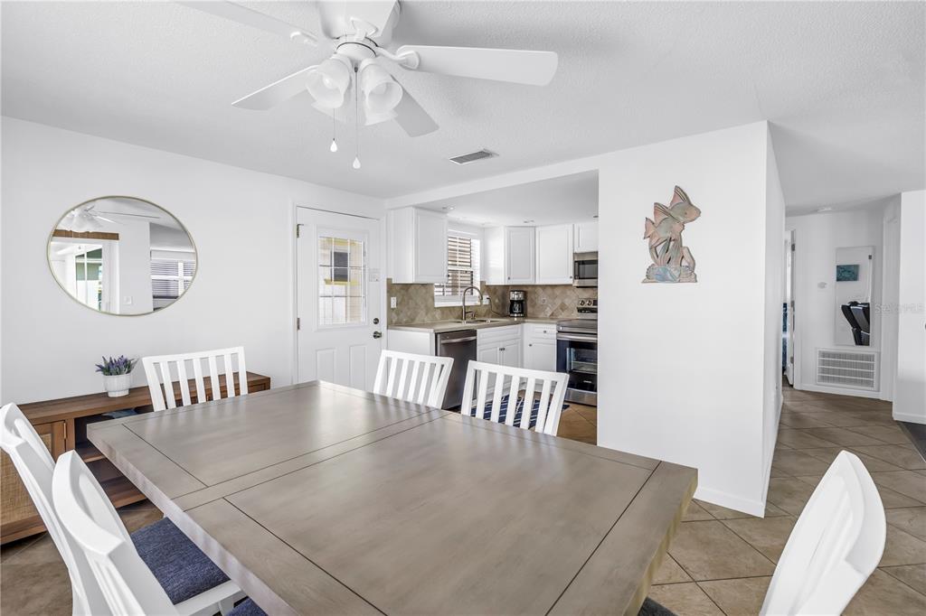 A dining area with a wooden table and white chairs opens into a kitchen — 6150 MIDNIGHT PASS ROAD UNIT V38, SARASOTA, FL