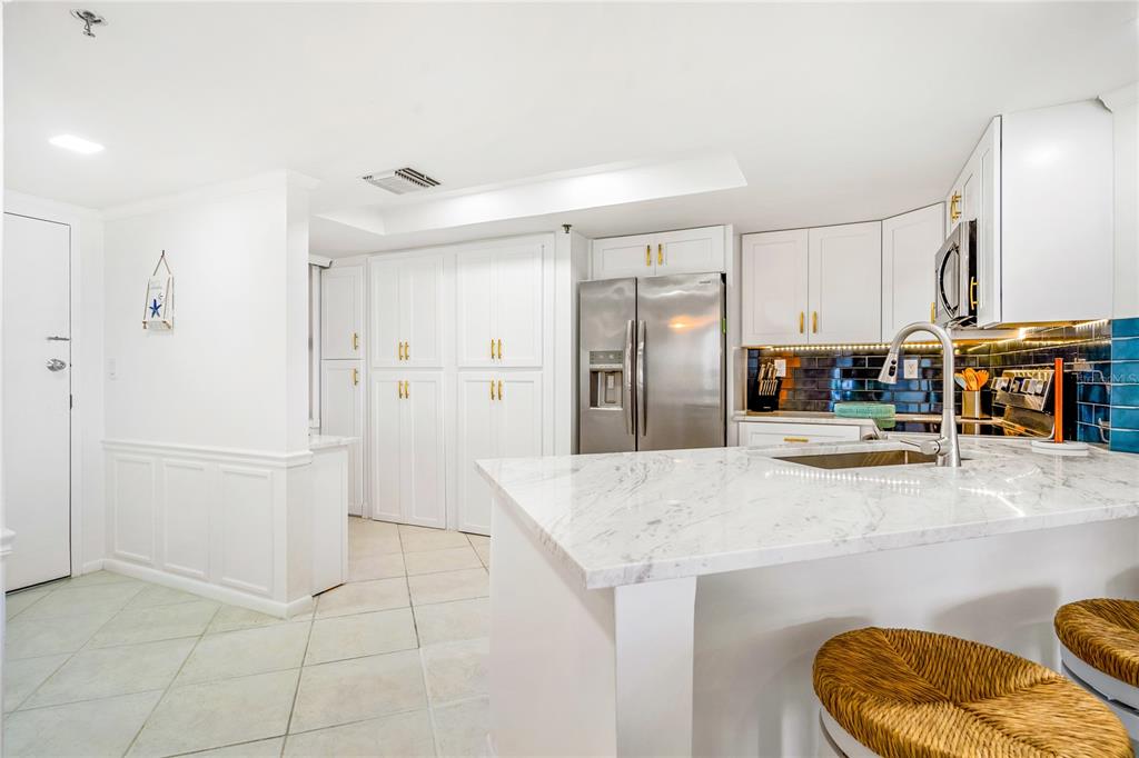 A white kitchen features a marble-topped island, stainless steel appliances, and blue tile backsplash — 3870 N HIGHWAY A1A UNIT 405, FORT PIERCE, FL