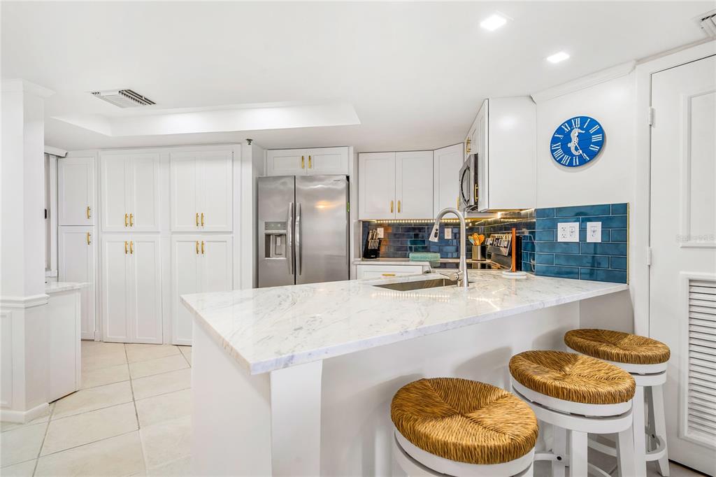 A kitchen features white cabinetry, a marble-topped island, stainless steel appliances, and blue tile backsplashes — 3870 N HIGHWAY A1A UNIT 405, FORT PIERCE, FL