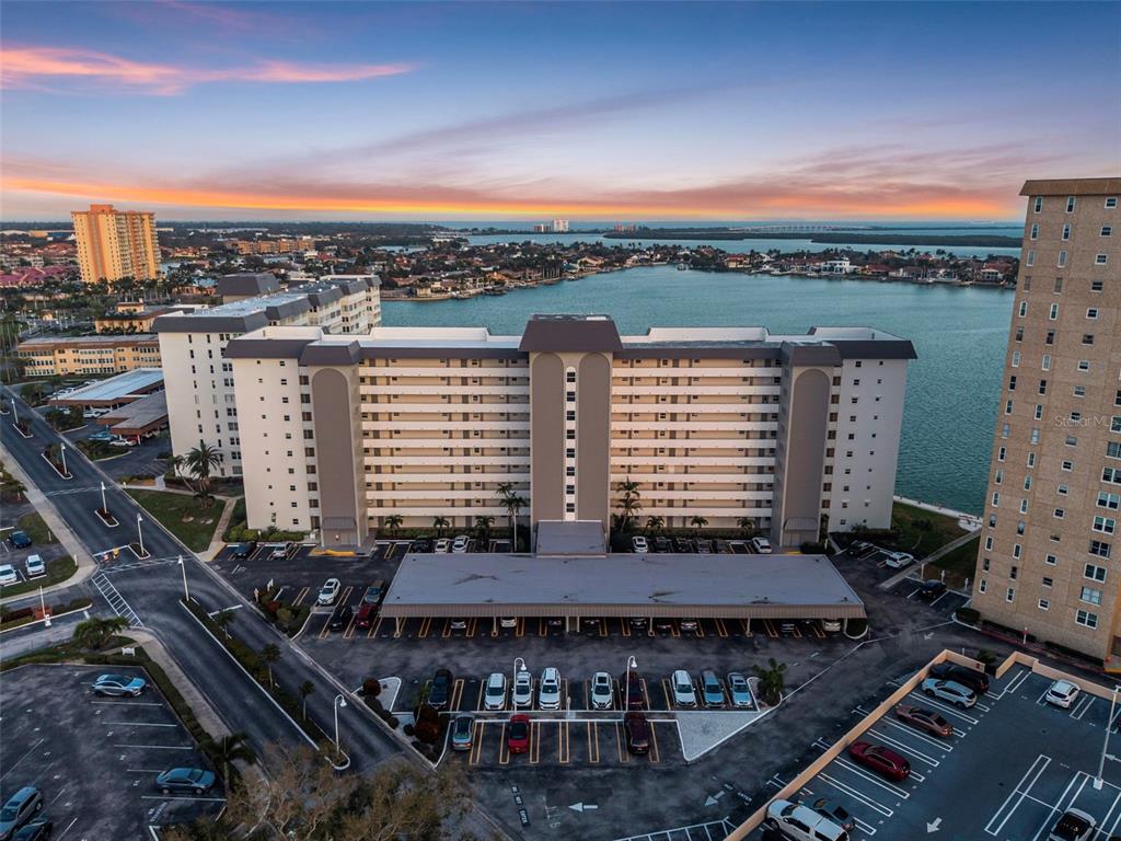 An aerial view shows a multi-story apartment building with a parking lot at sunset — 5130 BRITTANY DRIVE S UNIT 201, ST PETERSBURG, FL