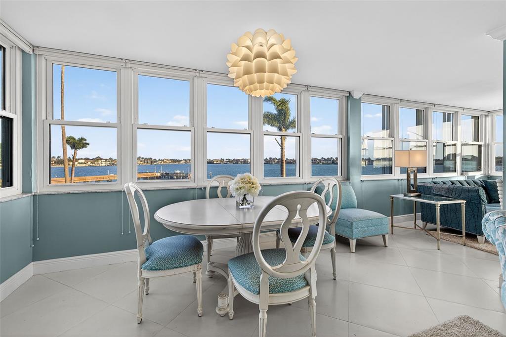 A sunroom with a dining set, light blue walls, and large windows overlooking the water — 5130 BRITTANY DRIVE S UNIT 201, ST PETERSBURG, FL