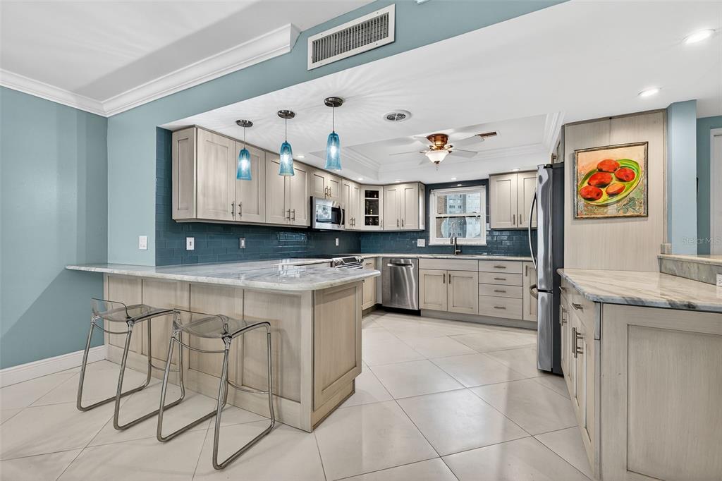 A kitchen features light wood cabinets, blue subway tile backsplash, marble countertops, and three bar stools — 5130 BRITTANY DRIVE S UNIT 201, ST PETERSBURG, FL