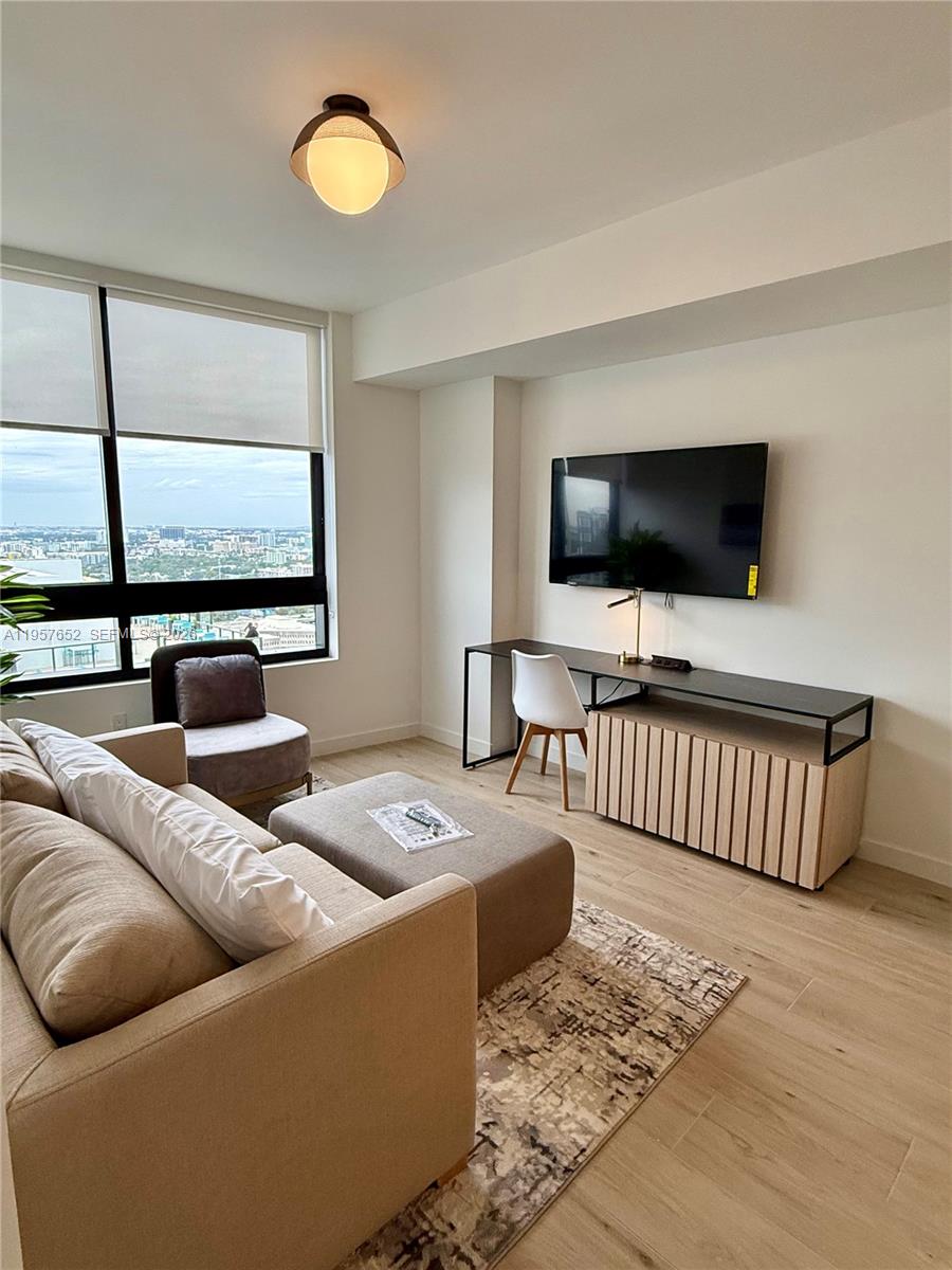 A living room features a sofa, a desk with a chair, and a wall-mounted television — 225 N Miami Ave # 3406, Miami FL 33128, MIAMI, FL