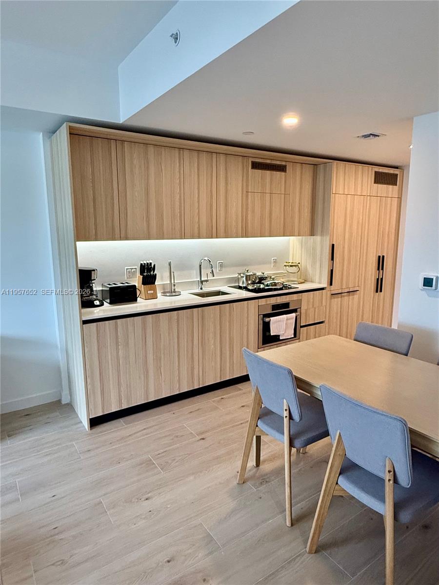 A modern kitchen features light wood cabinetry, integrated appliances, and a dining table with chairs — 225 N Miami Ave # 3406, Miami FL 33128, MIAMI, FL