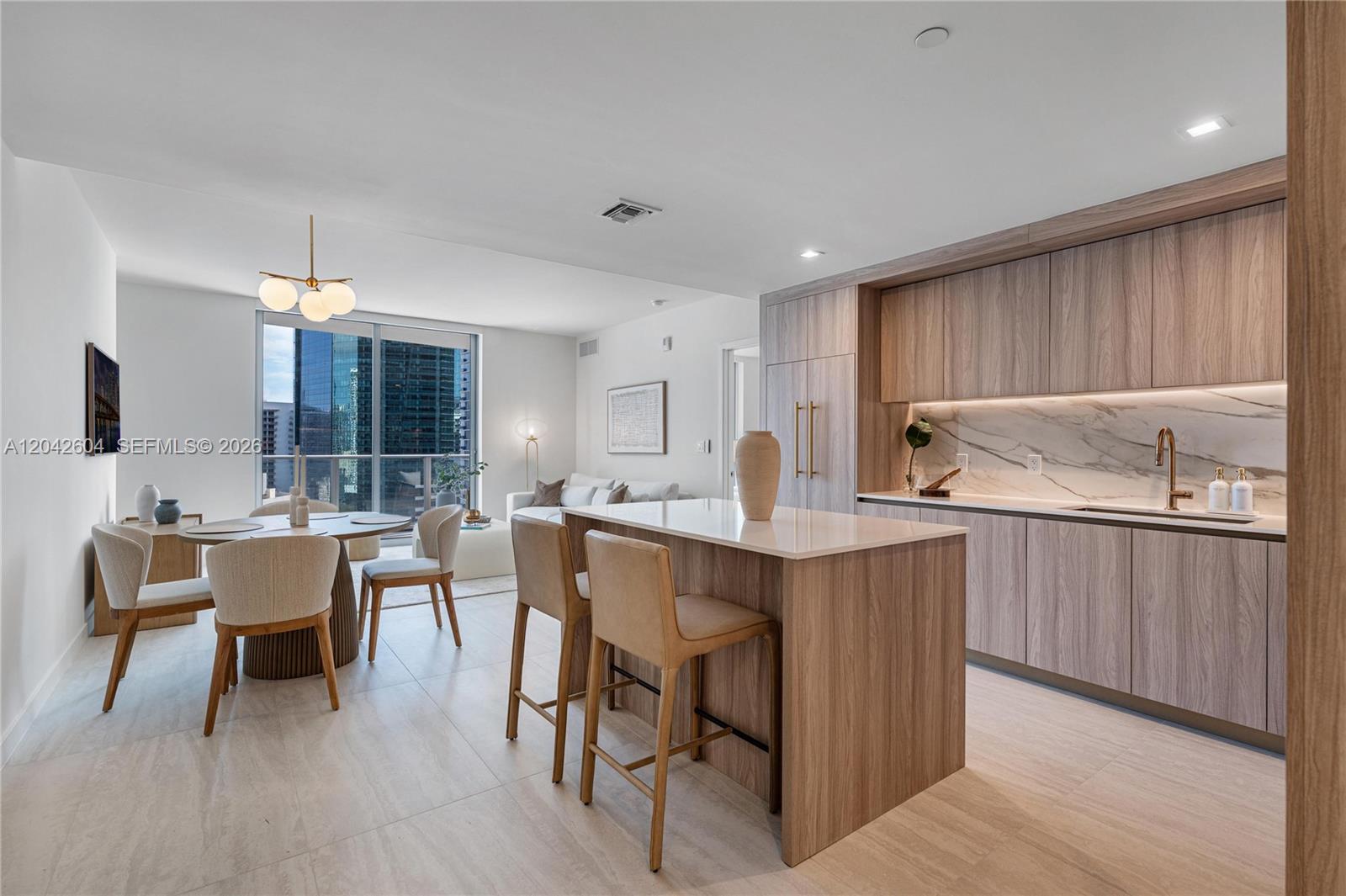 A modern kitchen and dining area features wood cabinetry, a stone island, and floor-to-ceiling windows — 77 SE 5th ST # 3001, Miami FL 33131, MIAMI, FL