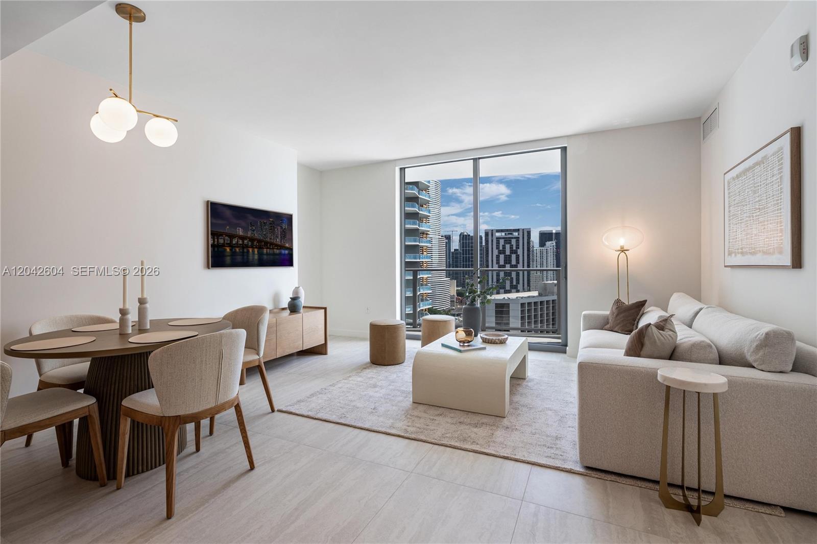 A modern living and dining area features neutral furniture, a large window, and city views — 77 SE 5th ST # 3001, Miami FL 33131, MIAMI, FL