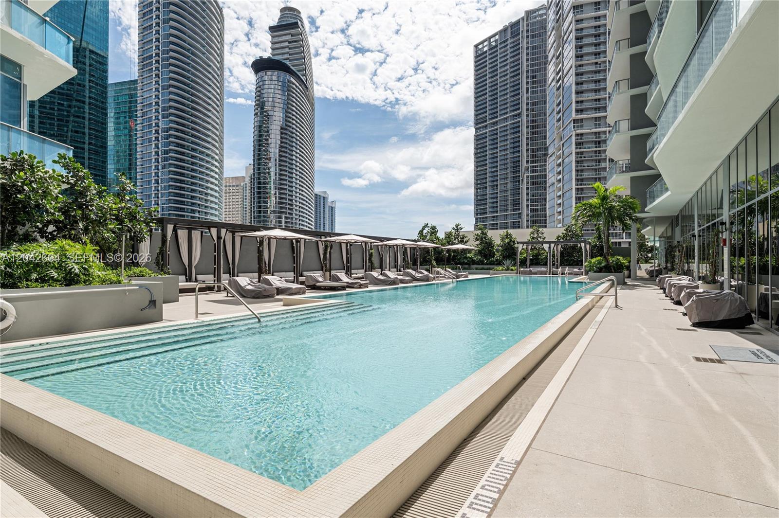 An outdoor swimming pool is surrounded by lounge chairs and tall residential skyscrapers — 77 SE 5th ST # 3001, Miami FL 33131, MIAMI, FL