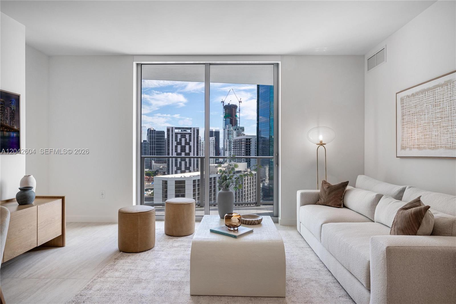 A modern living room features a light-colored sofa, coffee table, and floor-to-ceiling city views — 77 SE 5th ST # 3001, Miami FL 33131, MIAMI, FL
