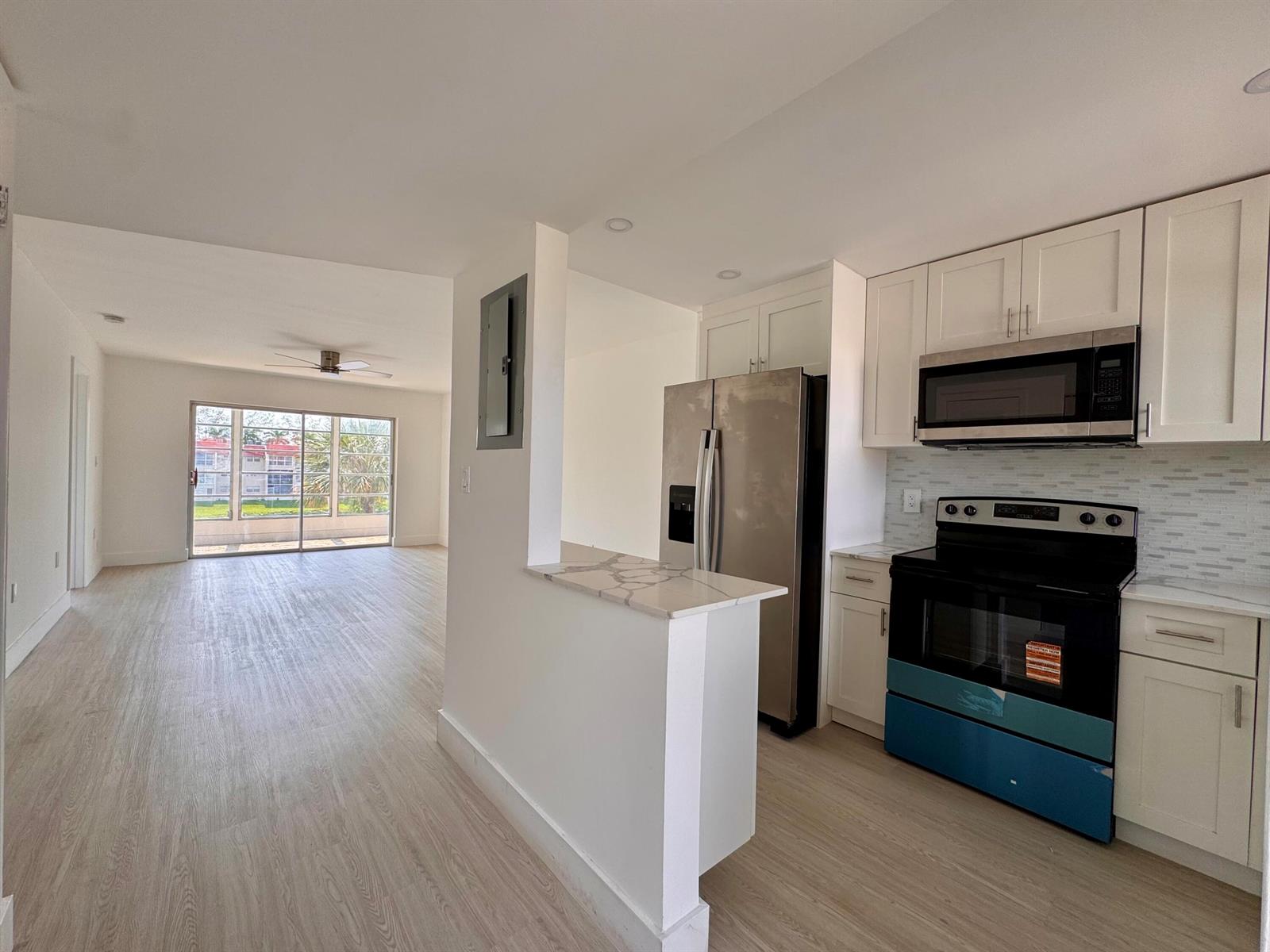 A kitchen with white cabinets and stainless steel appliances opens to a bright living area — 2831 E Sunrise Lakes Drive E # 311, Sunrise FL 33322, SUNRISE, FL