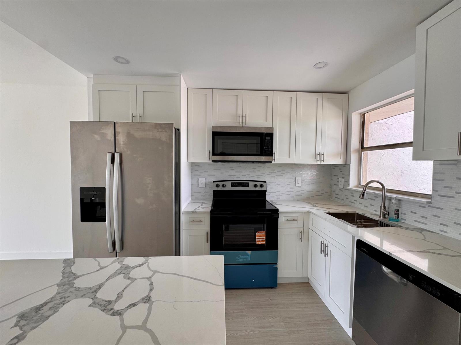 A kitchen features white cabinets, stainless steel appliances, and a marble-patterned countertop island — 2831 E Sunrise Lakes Drive E # 311, Sunrise FL 33322, SUNRISE, FL