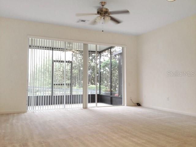 An empty room with beige carpet, a ceiling fan, and sliding glass doors to a lanai — 2551 STOCKTON DRIVE, SANFORD, FL