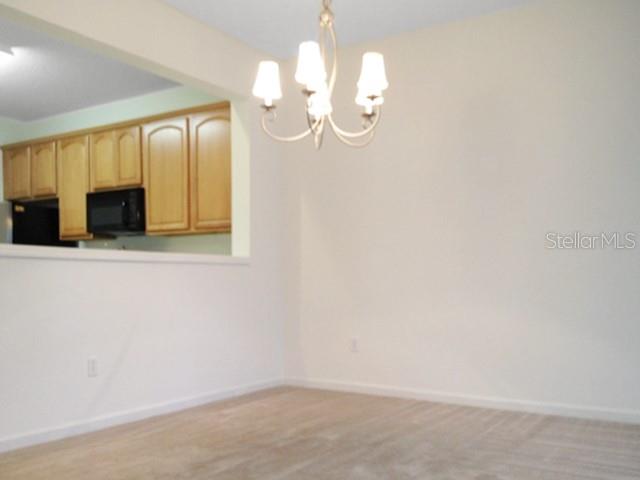A dining area features a chandelier, beige carpet, and a view into a kitchen with cabinets — 2551 STOCKTON DRIVE, SANFORD, FL