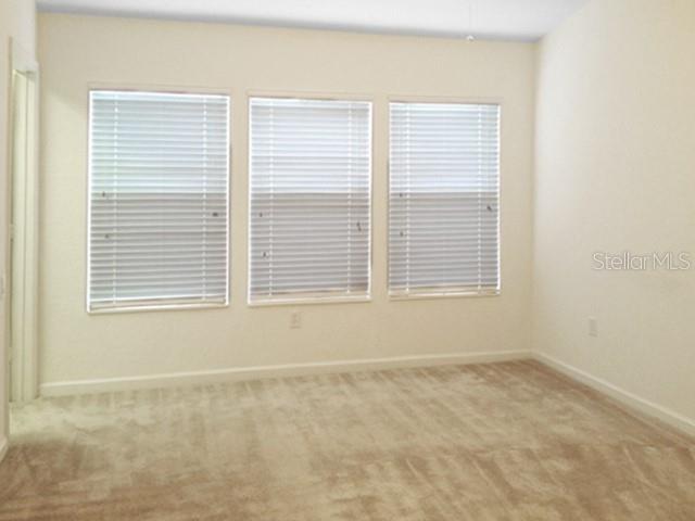 An empty room with beige carpeting and three windows covered by white horizontal blinds — 2551 STOCKTON DRIVE, SANFORD, FL
