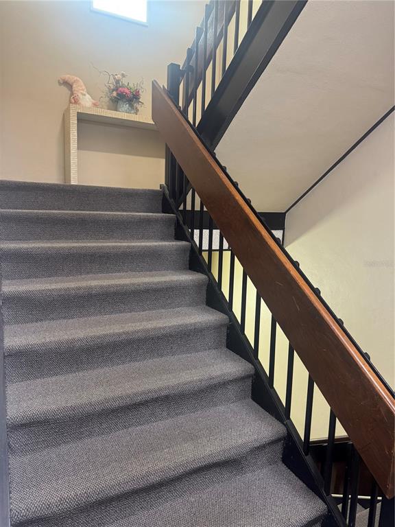 A carpeted staircase features a wooden handrail and black metal balusters leading to a landing — 1204 NW 69TH TERRACE UNIT B, GAINESVILLE, FL