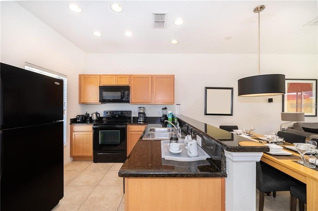 A kitchen with light wood cabinets, black appliances, and a dark granite breakfast bar — 3007 WHITE ORCHID ROAD, KISSIMMEE, FL