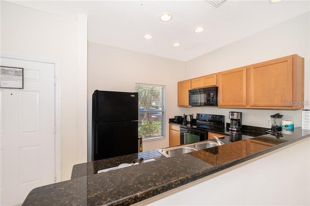 A kitchen features dark granite countertops, light wood cabinets, a black refrigerator, and recessed lighting — 3007 WHITE ORCHID ROAD, KISSIMMEE, FL
