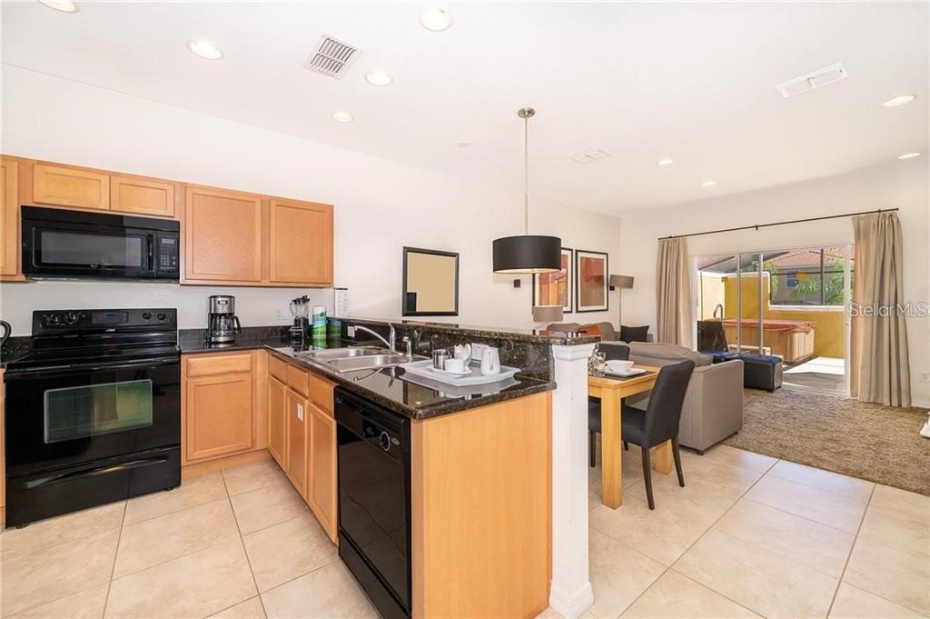 A kitchen with light wood cabinets and black appliances overlooks a dining and living area — 3007 WHITE ORCHID ROAD, KISSIMMEE, FL