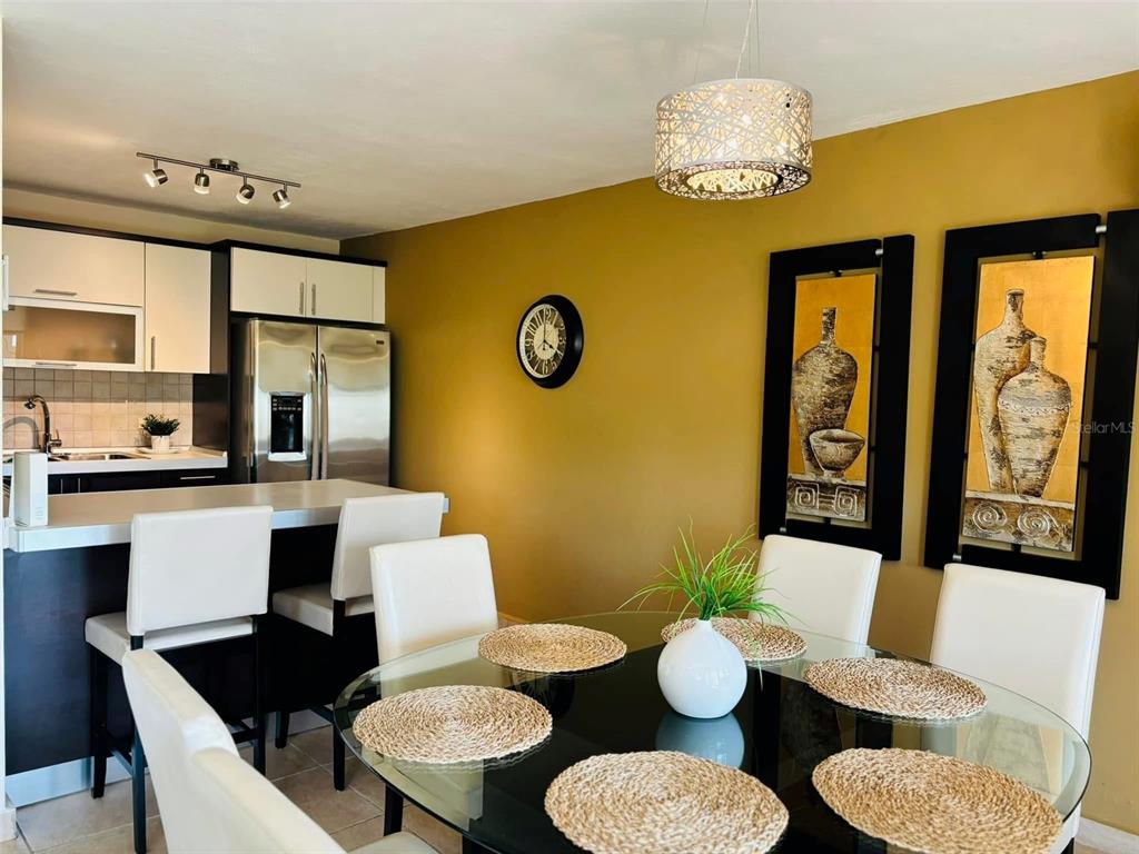 A dining area features a glass table, white chairs, and wall art near a kitchen — 1 COND. PUERTA DEL MAR, AGUADILLA, PR