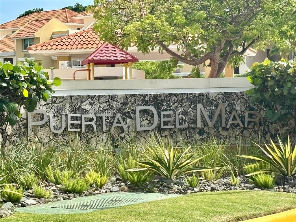 A stone sign reading Puerta Del Mar stands in front of a residential building — 1 COND. PUERTA DEL MAR, AGUADILLA, PR