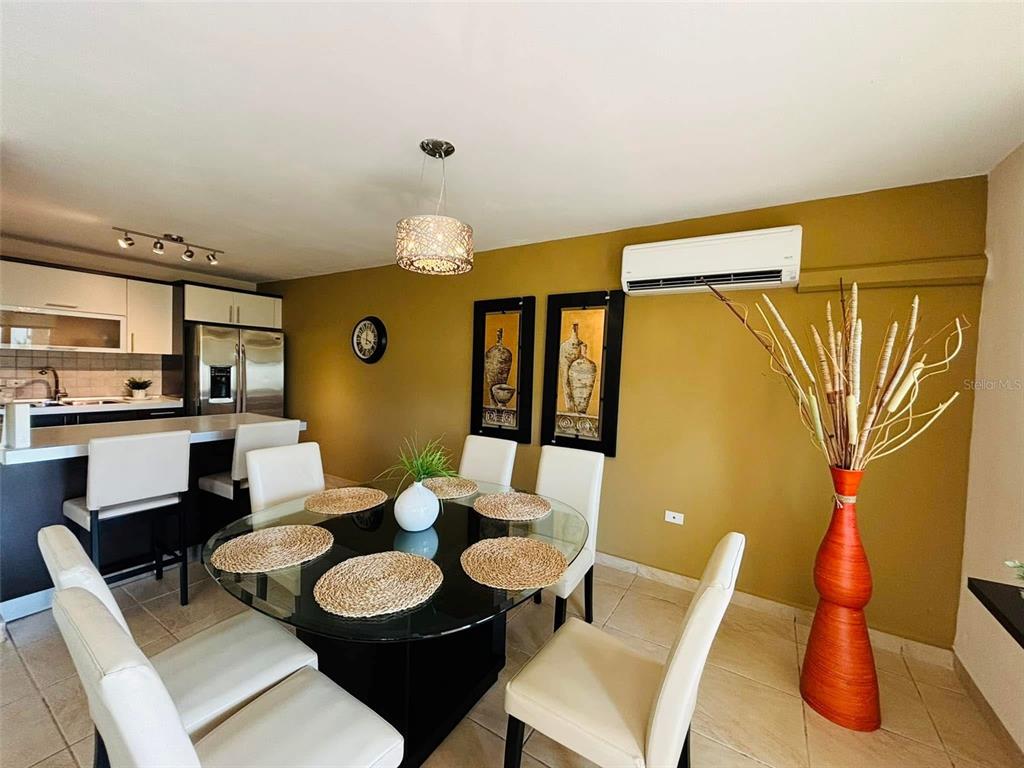 A dining area with a glass table, white chairs, and a tall orange floor vase — 1 COND. PUERTA DEL MAR, AGUADILLA, PR