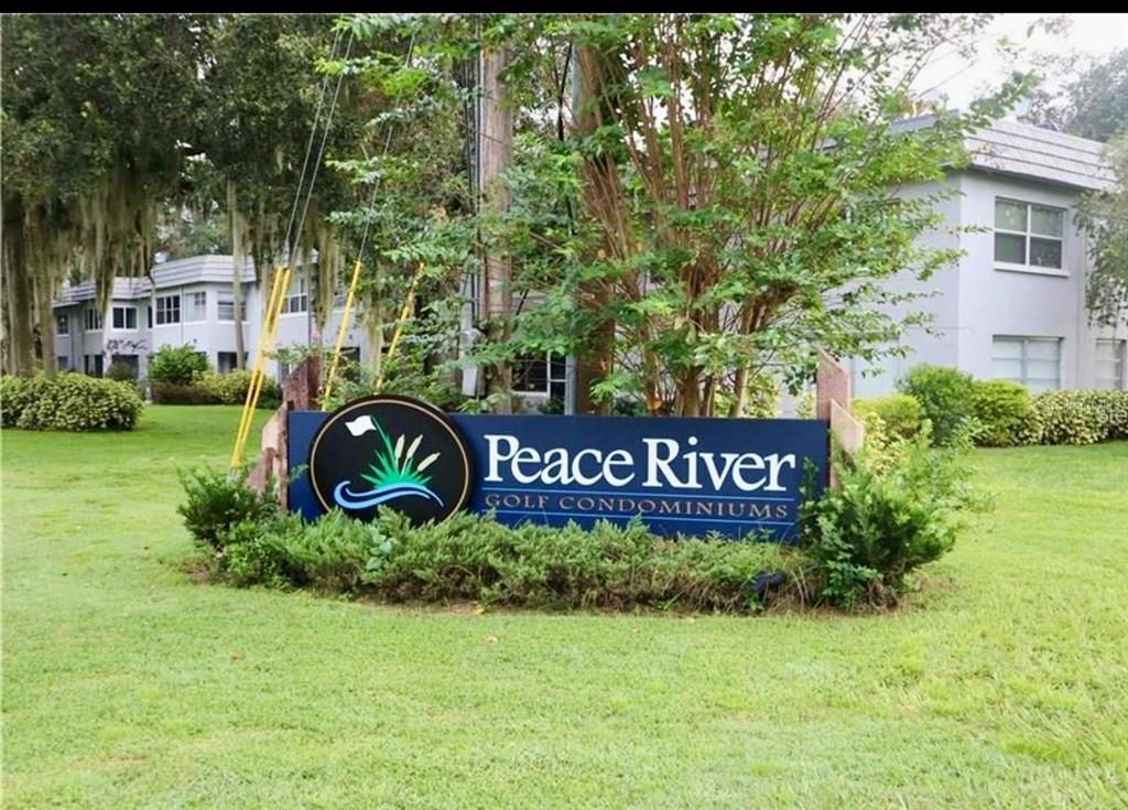 A sign for Peace River Golf Condominiums stands in a grassy yard before apartment buildings — 220 N IDLEWOOD AVENUE UNIT 204, BARTOW, FL
