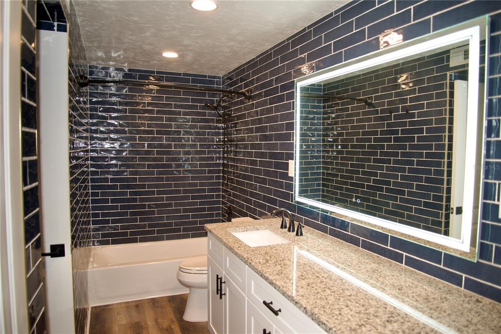 A bathroom features dark blue subway tile walls, a granite vanity, and a lighted mirror — 220 N IDLEWOOD AVENUE UNIT 204, BARTOW, FL