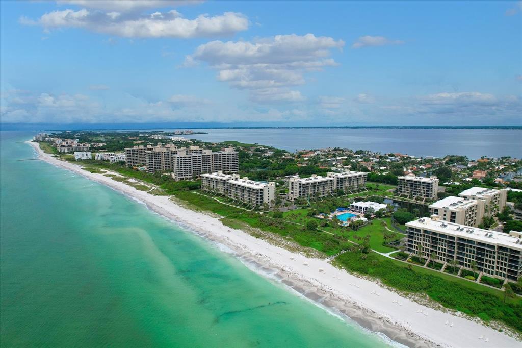 An aerial view of beachfront condominiums along a coastline with turquoise water and a blue sky — 1105 GULF OF MEXICO DRIVE UNIT 402, LONGBOAT KEY, FL