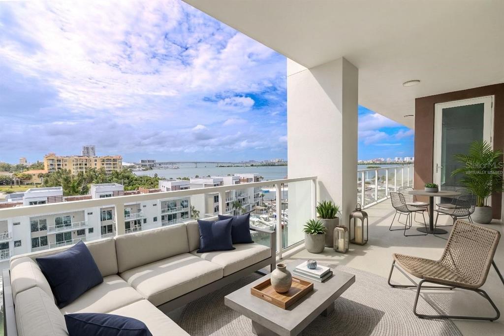 A furnished balcony overlooks a bay with a bridge and nearby buildings under a cloudy sky — 920 N OSCEOLA AVENUE UNIT 703, CLEARWATER, FL