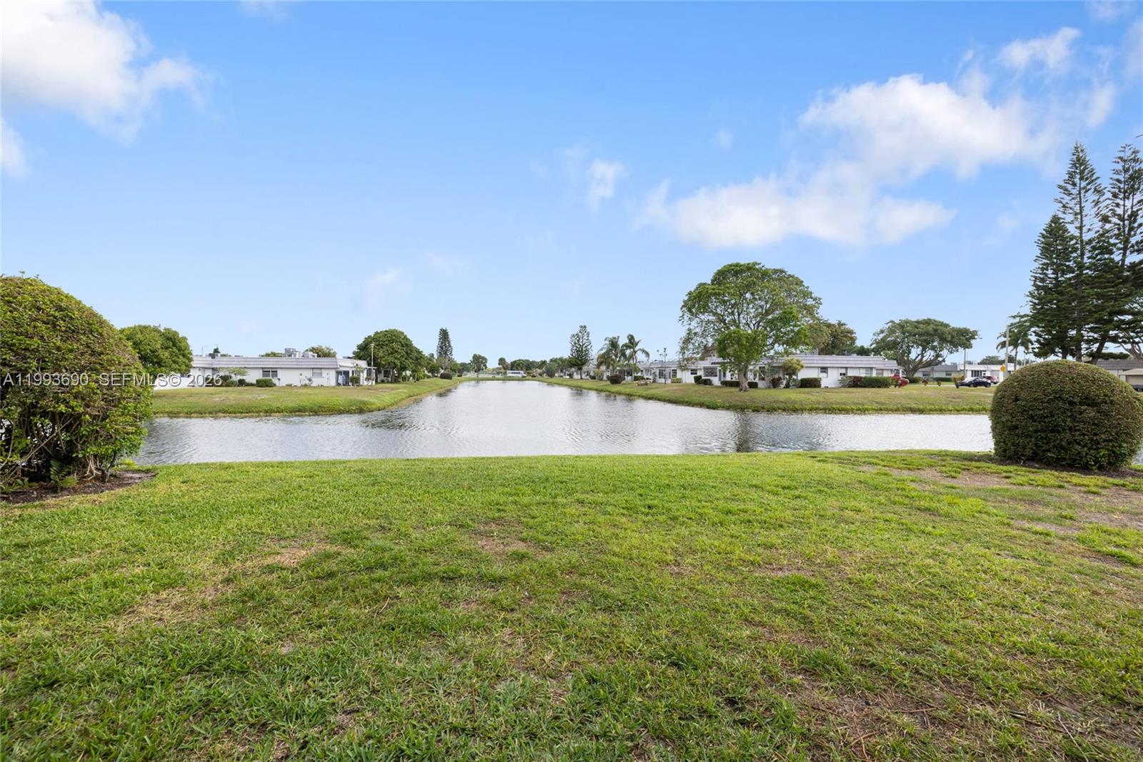 A grassy lawn overlooks a narrow canal lined with residential buildings under a blue sky — 72 Monaco B # 72, Delray Beach FL 33446, DELRAY BEACH, FL