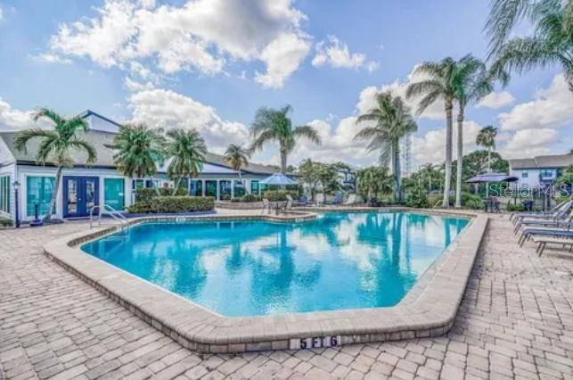 A swimming pool with a brick deck and palm trees sits in front of a building — 115 112TH AVENUE NE UNIT 810, ST PETERSBURG, FL