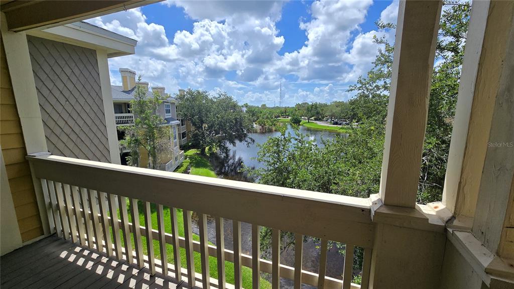 A balcony view overlooks a pond and surrounding apartment buildings under a cloudy blue sky — 115 112TH AVENUE NE UNIT 810, ST PETERSBURG, FL