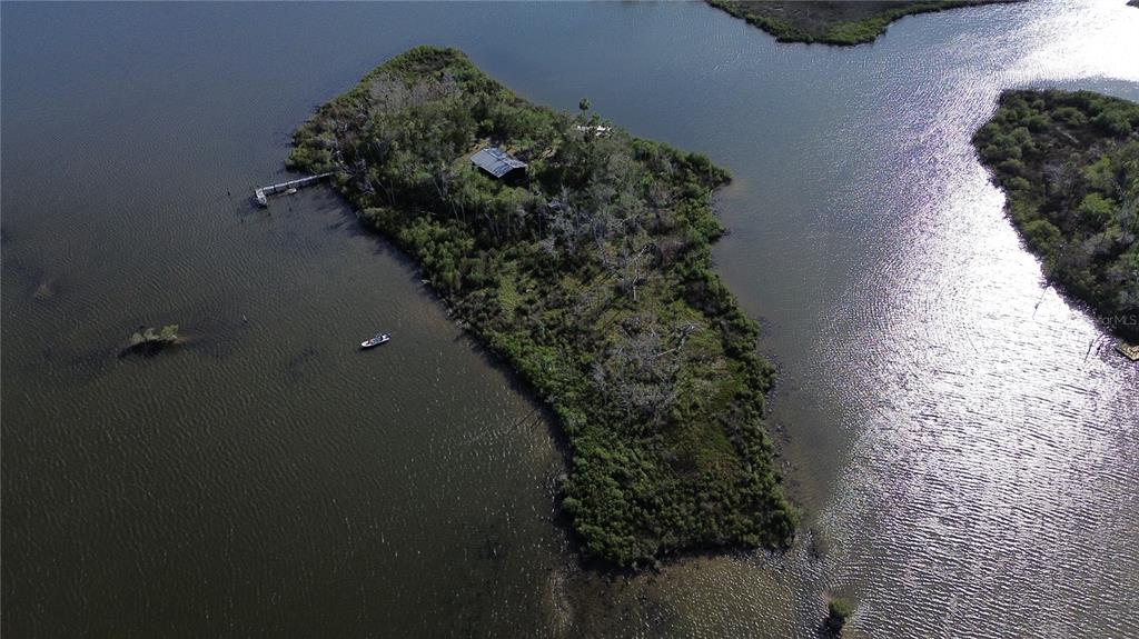 An aerial view shows a small, wooded island featuring a cabin and a private dock — 7472 W THUNDERBIRD ISLAND, HOMOSASSA, FL