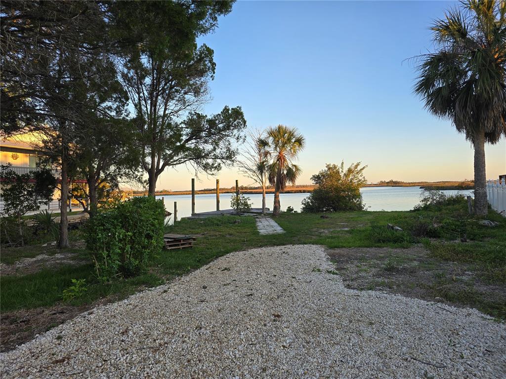 A gravel driveway leads to a grassy yard with a dock overlooking a calm waterway — 7472 W THUNDERBIRD ISLAND, HOMOSASSA, FL