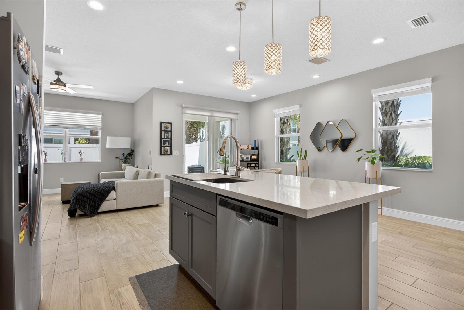 A kitchen island with a stainless steel dishwasher sits before an open-concept living area — 1835 Sandpiper Pointe Place, Deerfield Beach FL 33442, DEERFIELD BEACH, FL