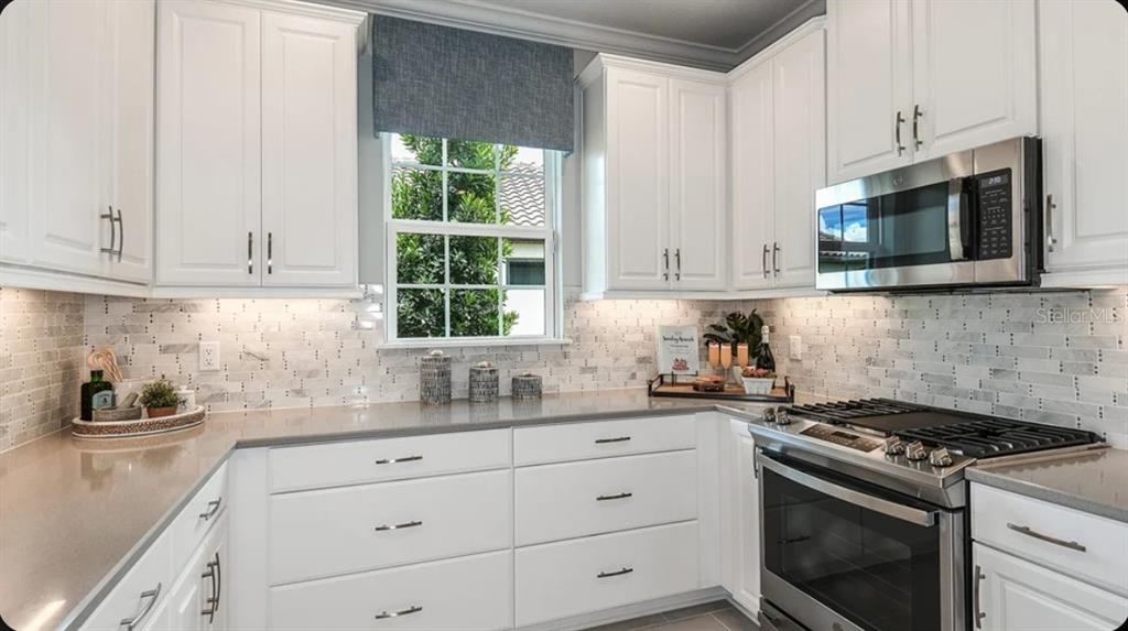 A kitchen features white cabinetry, stainless steel appliances, a gray countertop, and a tiled backsplash — 3205 TORTA COURT, BRADENTON, FL