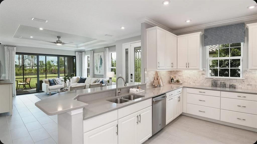A kitchen with white cabinets and gray countertops overlooks an open-concept living room and patio — 3205 TORTA COURT, BRADENTON, FL