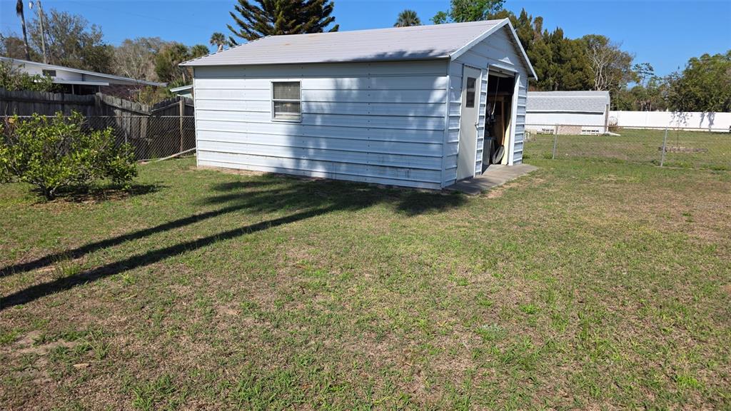 A white metal shed with a window and a door sits in a grassy yard — 707 JANE AVENUE, NEW SMYRNA BEACH, FL