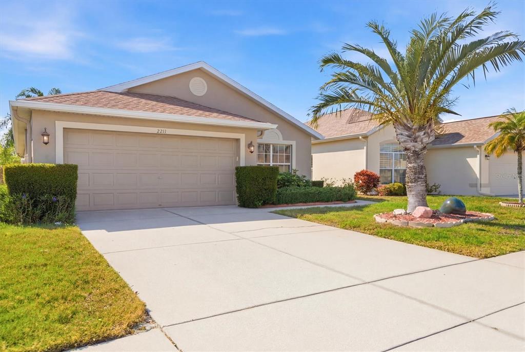A single-story suburban house with a beige exterior, a two-car garage, and a palm tree — 2211 PLEASANT HILL LANE, HOLIDAY, FL