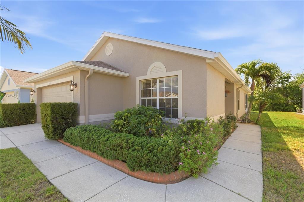A beige single-story house with a garage, a concrete walkway, and landscaped bushes — 2211 PLEASANT HILL LANE, HOLIDAY, FL