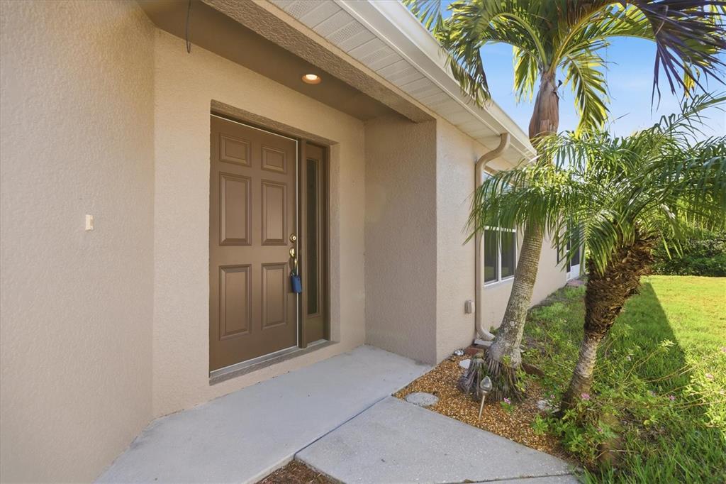 A brown front door with a side window is set into a beige stucco exterior — 2211 PLEASANT HILL LANE, HOLIDAY, FL