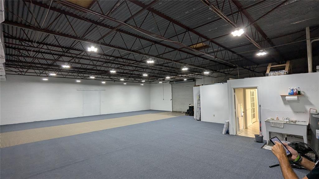A large, open warehouse space features gray carpeting, white walls, and exposed ceiling rafters — 11920 31ST COURT N, ST PETERSBURG, FL