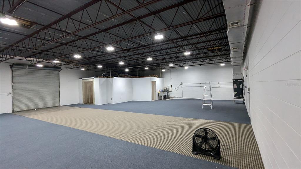 A large, open commercial space features a roll-up door, exposed ceiling, and carpeted flooring — 11920 31ST COURT N, ST PETERSBURG, FL