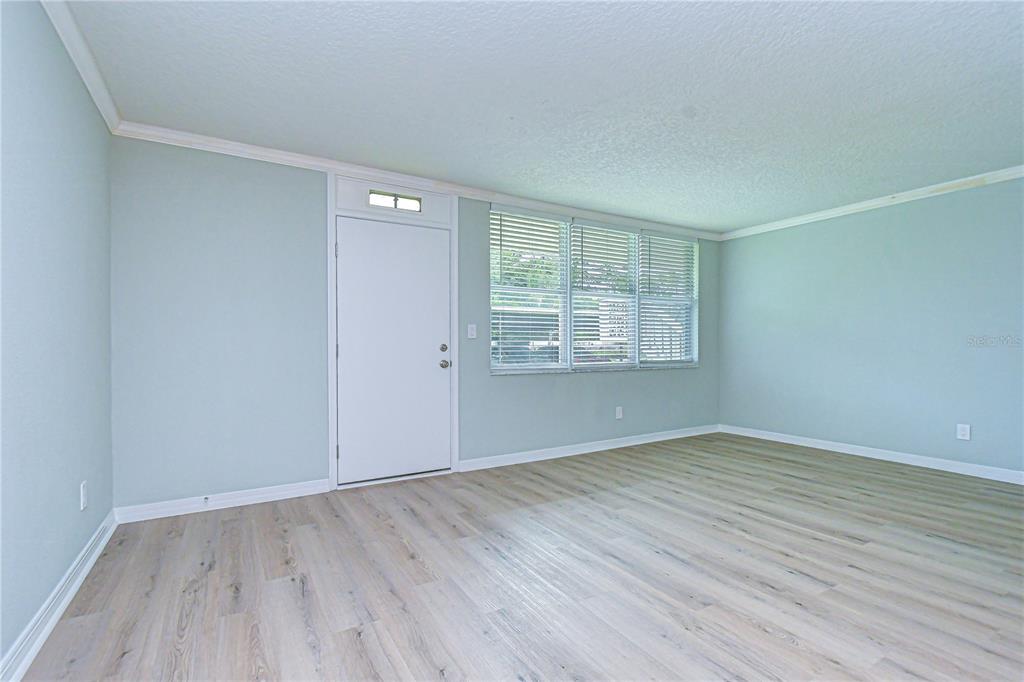 An empty room with light blue walls, wood-look flooring, and a white entry door — 4720 LOCUST STREET NE UNIT 118, ST PETERSBURG, FL