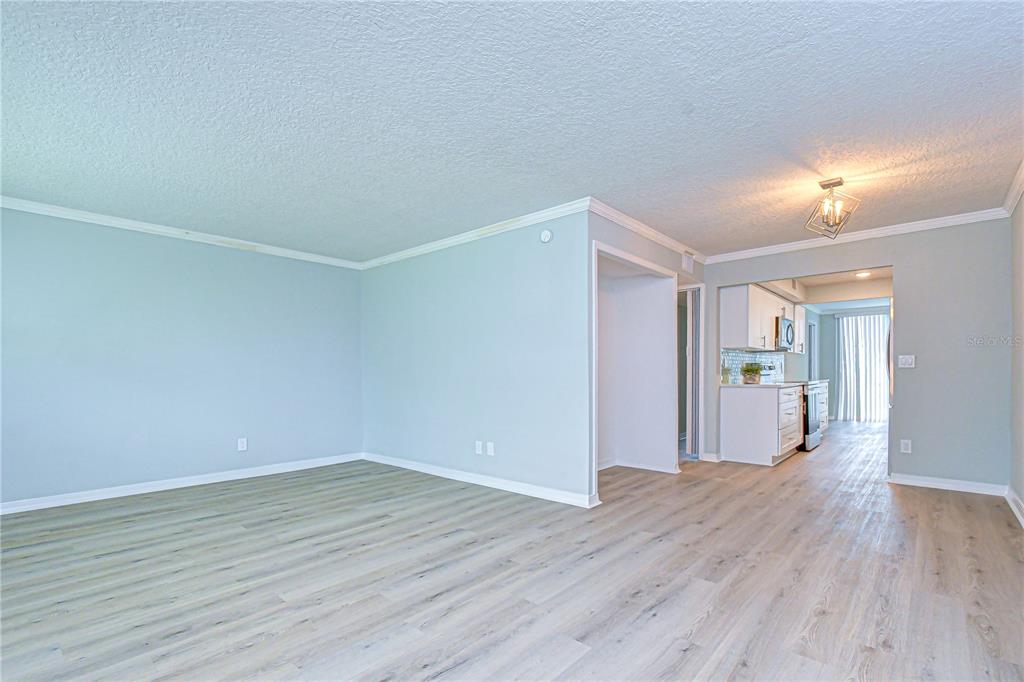 An open-concept living area with light-colored walls and wood-look flooring leads into a kitchen — 4720 LOCUST STREET NE UNIT 118, ST PETERSBURG, FL