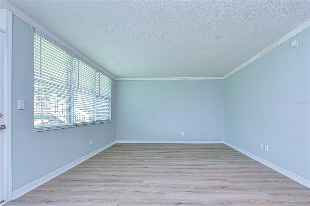 An empty room features light-colored wood-look flooring, pale blue walls, and large windows with blinds — 4720 LOCUST STREET NE UNIT 118, ST PETERSBURG, FL